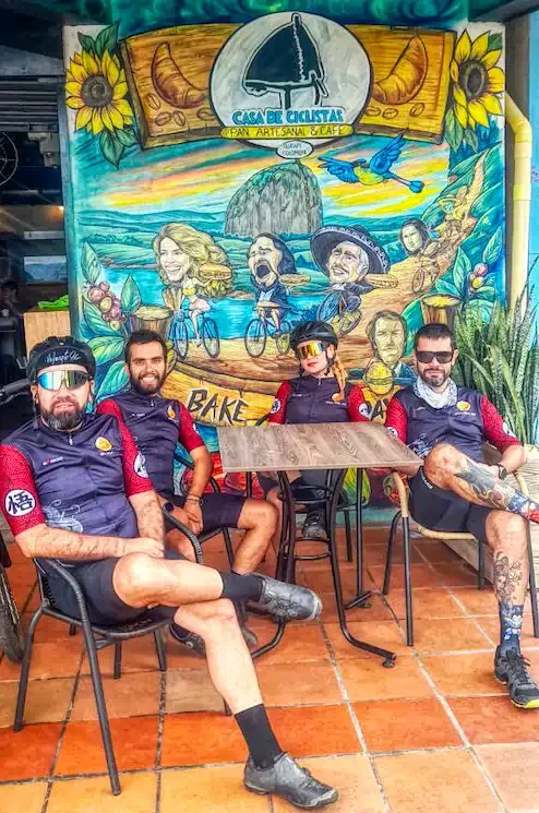 Group of cyclists sitting at Casa de Ciclistas in front of the restaurant mural, Guatapé Colombia