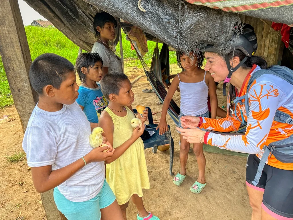 Johana in MBC jersey speaking with indigenous children holding baby chicks, Amazon community Colombia